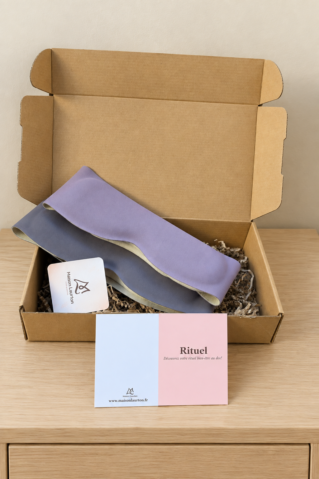 Masques lestés L’Étreinte en teintes lilas et grise, présentés dans leur coffret sur une table de chevet claire.